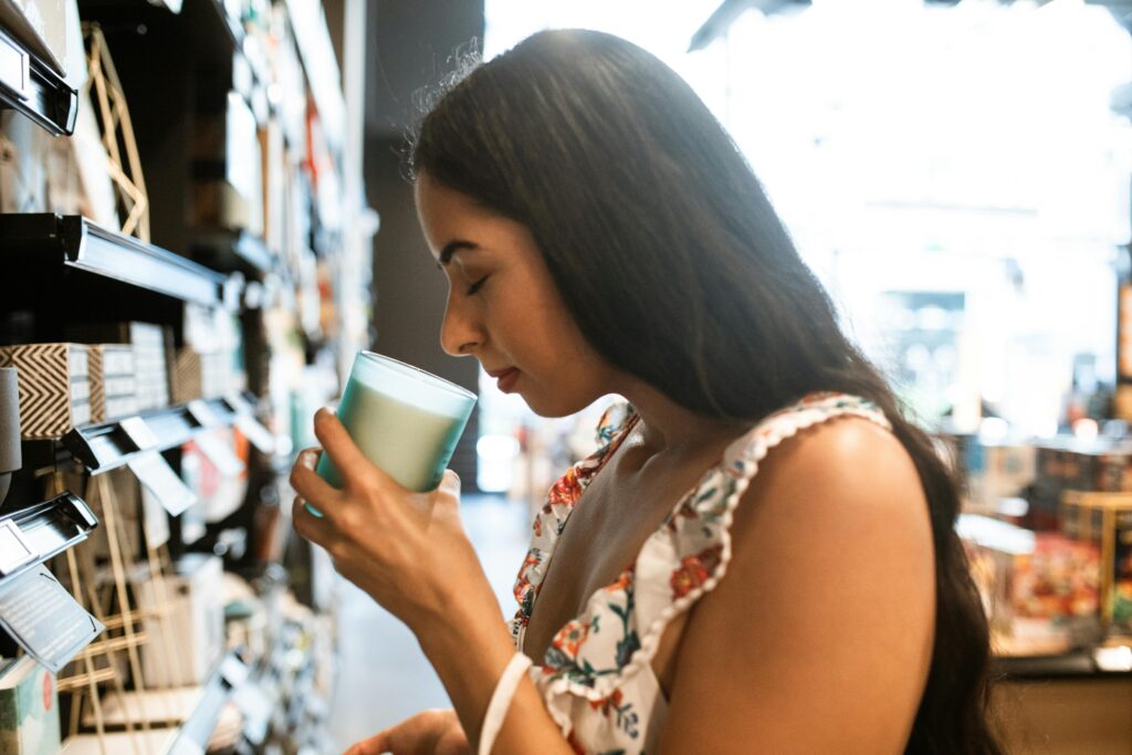 Young woman smelling a scented candle while shopping in a well-lit store.